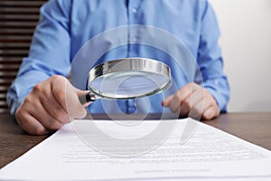 Man looking at document through magnifier at wooden table, closeup. Searching concept