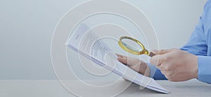 Man looking at documents through magnifier at wooden table, closeup. Banner design with space for text