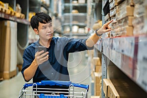 Man looking at his mobile phone and shopping in warehouse store