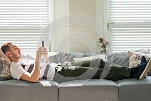 Man looking his smart phone while, lying on the couch at home