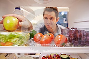 Man Looking Inside Fridge Full Of Food And Choosing Apple