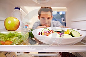 Man Looking Inside Fridge Full Of Food And Choosing Salad