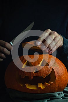 Man looking into Jack`s lantern orange pumpkin for traditional autumn holiday Halloween. One hand is holding pumpkin cap