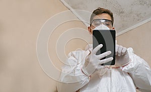 a man looking at a musty white wall. Makes notes about cleaning on your phone. Specialist of sanitary and epidemiological service