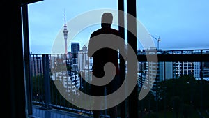 Man looking out balcony on Auckland city skyline at dusk