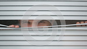 Man looking out the window through the blinds to the street, spying. suspected