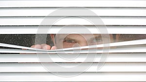 Man looking out the window through the blinds to the street, spying. suspected