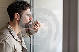 Man Looking Out a Window With Hand on Face