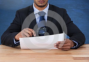 Man looking at paper with magnifying glass at desk