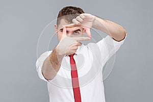 Man looking through photo frame made of hands, focusing and cropping image