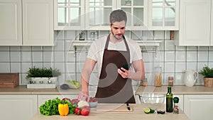 Man looking at recipe for vegan salad using smartphone while standing in kitchen