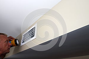 Man Looking into a Rectangle Home Wall Vent with a Flashlight