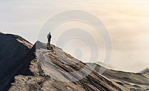 Man looking at sea of clouds on top of a volcano mountain crest in Bromo, Java, Indonesia