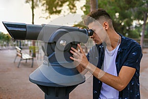 Man looking through a telescope while standing in a clearing surrounded by lush green trees