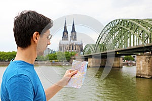 Man looking to his paper map in his hand with Cologne Cathedral and bridge on Rhine river, Germany. Travel in Europe.