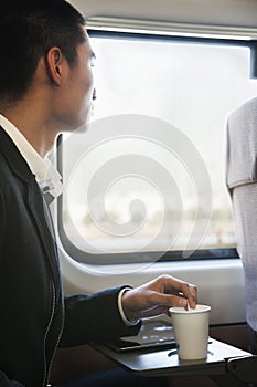 Man Looking Through Train Window While Stirring His Coffee