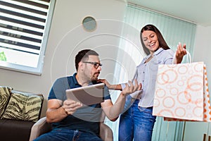 Man looking troubled when shopaholic woman arriving home with shopping bags