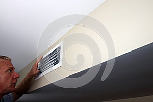 Man Looking into a Wall Home Air Vent While Holding One Hand Up