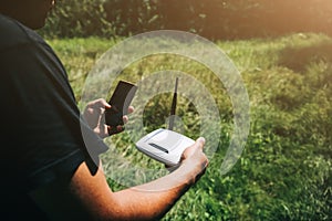 Man is looking for wi-fi signal in the nature. Guy is lost and holding router with smartphone  in his hands searching for internet