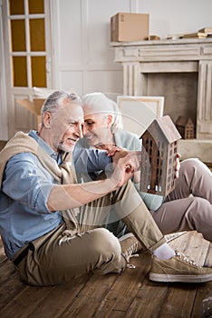 Man looking at wooden house model in hands with smiling wife