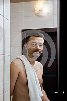 A man looks in the bathroom mirror in the morning with a towel on his shoulder