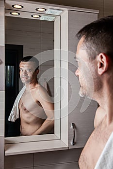 A man looks in the bathroom mirror in the morning with a towel on his shoulder