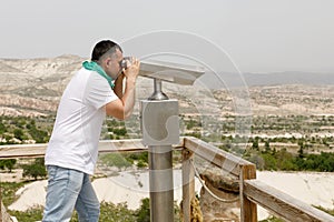 A man looks through binoculars, enjoying a beautiful view from a high mountain