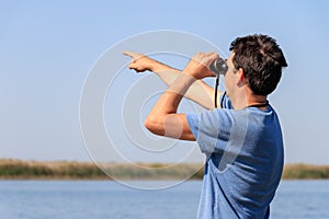 A man looks through binoculars at the river