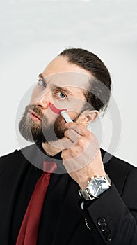 The man looks at the camera and paints with lipstick on his cheek. You should not be afraid of other people's opinions.