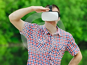 Man looks into the distance in the virtual reality glasses on background of green forest