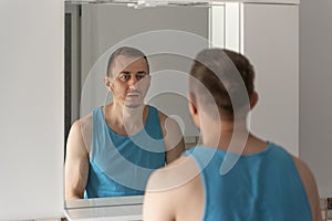 Man looks at himself in bathroom mirror. View over the shoulder. Morning routine. Sleepy tired man in bathroom