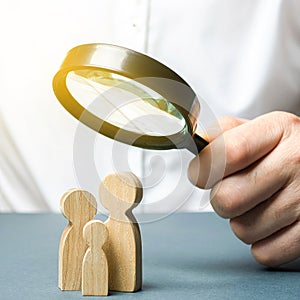 A man looks through a magnifying glass at a family figure. The study of family composition and demographic situation. Statistical