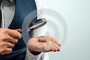 A man looks through a magnifying glass at a stack of coins in his palm. Small salary, financial crisis, bankruptcy photo