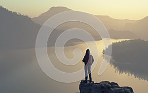 A man looks over the top of the mountain lake and forest.