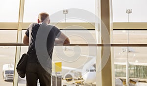 A man looks at a plane through a glass wall at the airport