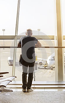 A man looks at a plane through a glass wall at the airport