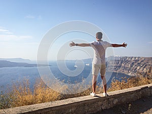 A man looks at the sea with his hands spread wide on a hot summer day