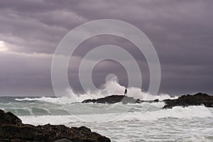 Man looks for shellfish on rocks in stormy sea