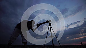 Man looks through a telescope at the evening sky