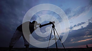 Man looks through a telescope at the evening sky