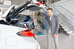 Man looks at the trunk of new car in showroom