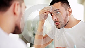 Man with lotion or toner cleaning face at bathroom