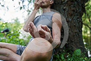 Man in lotus pose sitting on green grass near the tree and doing breathing exercise