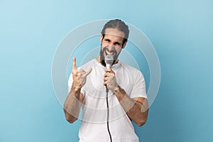 Man loudly singing song holding microphone in hand, having fun resting in karaoke, showing rock sign