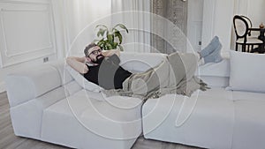 Man lounging on white couch in stylish living room with hardwood flooring