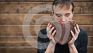 Man with love enjoys aroma of freshly baked rye bread in shape heart, valentine gift, brown background with copy space