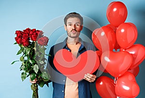 Man in love wishing happy Valentines day, waiting for kiss on romantic date, holding red roses, red heart and balloons