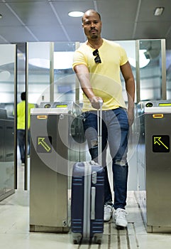 Man with luggage and headphone walk near baffle gate of subway