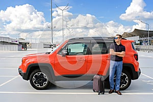 A man with luggage stands near his car in the parking lot.