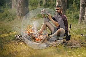 Man lumberjack with beard sharpen axe at bonfire